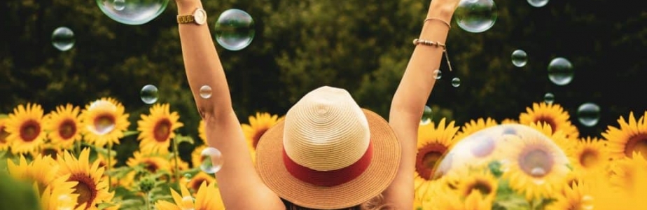 Woman raising arms amongst sunflowers and bubbles