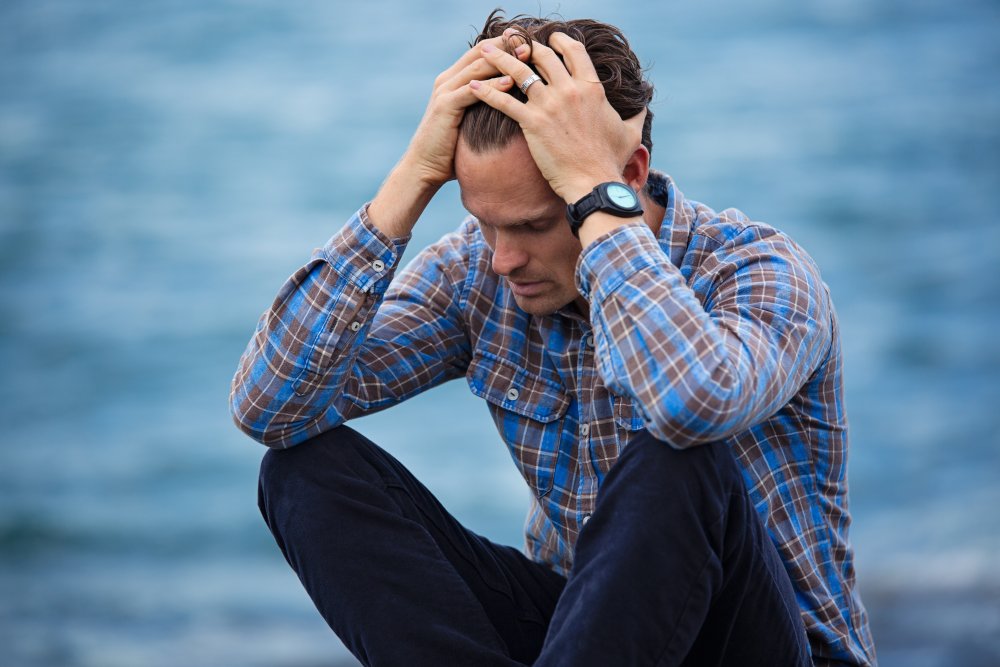 man in front of body of water holding head