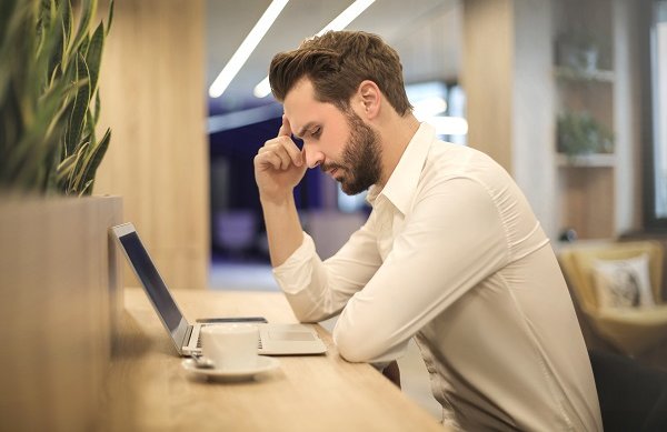 man at coffee shop thinking while looking at computer