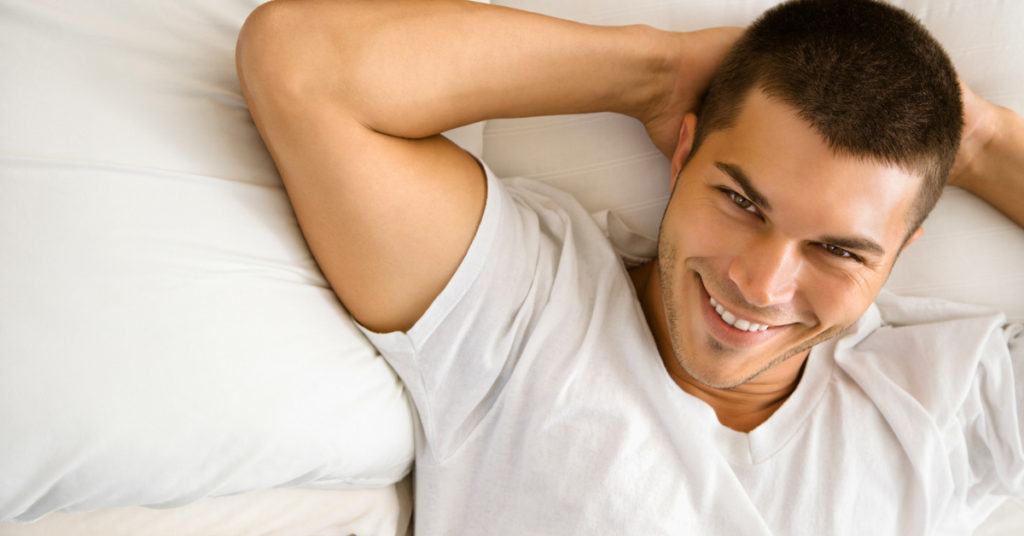 man laying on bed smiling looking at camera