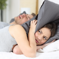 Woman covering head with pillow while man snores behind her