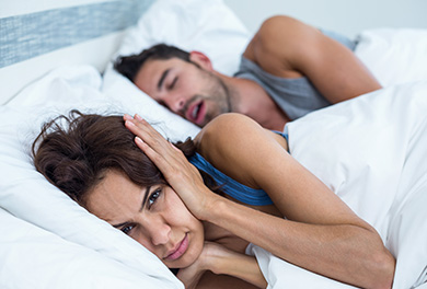 Woman in bed covering ears while man is snoring