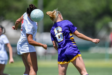 Two girls on opposing soccer team going for a header