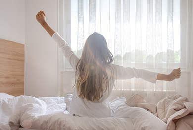 Woman waking and stretching in the sunlight through the window